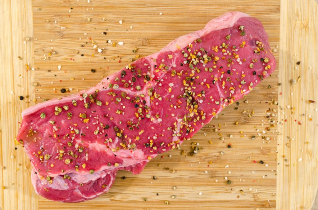 Close-up of a raw steak with spices on a wooden cutting board, perfect for cooking inspirations.